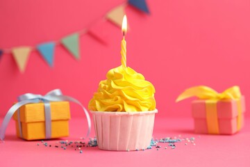 Tasty cupcake with burning candle and gift boxes on pink background