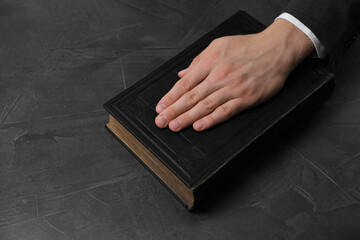 Man taking oath with his hand on Bible at black table, closeup