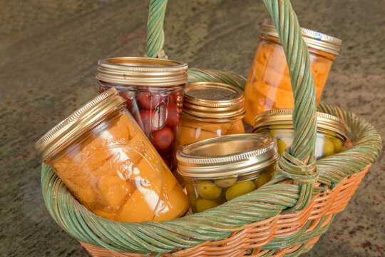 Wicker basket of home canned foods (peaches, olives and cherries) on a granite countertop in a kitchen.