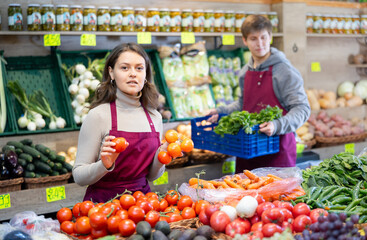 Female supermarket employee selling ripe tomatoes in the produce department
