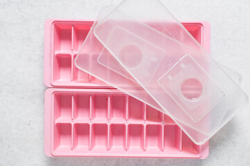 Overhead view of pink ice cube tray with a lid, top view of trendy pink ice cube trays on a white marble countertop