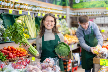 Positive girl seller with cabbage in her hands in the grocery department of the supermarket