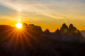 Sunset in the mountains. Red and orange burning sky horizon behind the alpine mountain range. Rocky mountain peaks of the Dolomites at sunset and dawn at sunrise light sunrays going through the clouds