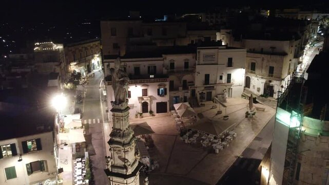 Vis&atilde;o a&eacute;rea da cidade de Ostuni &agrave; noite, It&aacute;lia. As ruas iluminadas e a arquitetura branca se destacam sob o c&eacute;u noturno, criando uma cena m&aacute;gica e encantadora