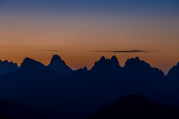 Sunset in the mountains. Red and orange burning sky horizon behind the alpine mountain range. Rocky mountain peaks of the Dolomites at sunset and dawn at sunrise light sunrays going through the clouds