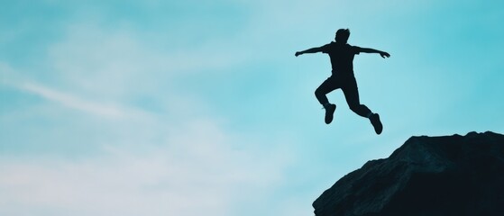 person jumping off a rock against a blue sky