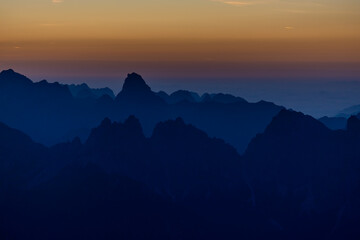 Sunset in the mountains. Red and orange burning sky horizon behind the alpine mountain range. Rocky mountain peaks of the Dolomites at sunset and dawn at sunrise light sunrays going through the clouds