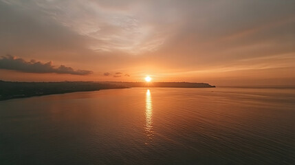 Naklejka premium Aerial View of Coastal Sunset: Golden Sun Descends Over Calm Ocean Waters and Silhouette Coastline, Creating a Serene and Breathtaking Scene