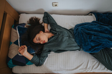 A relaxed woman sleeping comfortably on a bed, wrapped in a blue blanket. The peaceful atmosphere conveys serenity and restfulness, highlighting the importance of proper rest and relaxation.