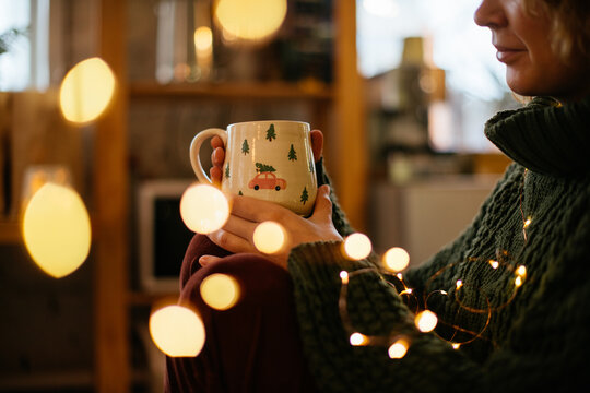 Woman holding a cozy Christmas mug, creating holiday warmth. Warm and nostalgic Christmas image of woman with festive mug and twinkling lights