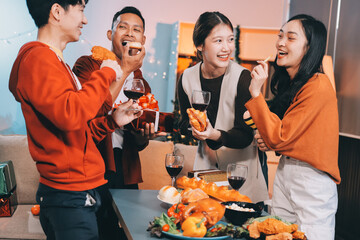 Group of young Asian man and women as friends having fun at a New Year's celebration, holding gift boxes standing by Christmas tree decoration, midnight countdown Party at home with holiday season.