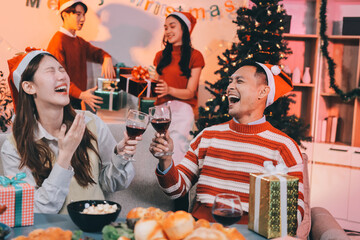 Group of happy Asian friends celebrating Christmas and decorate the Christmas tree indoors. Beauty woman with Christmas Gifts. New Year party. Woman hands decorate Christmas tree red ball, bauble.