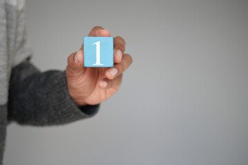 A hand is holding a blue block that has the number one inscribed on it against a neutral background