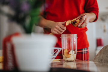 A person in a red sweater peels and slices apples for a nutritious smoothie. The kitchen setting adds warmth and a homely atmosphere, embodying healthy living and simple home cooking.