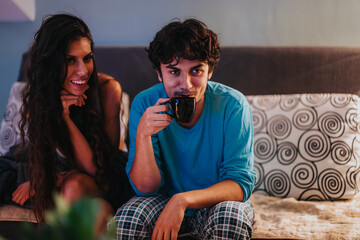 A couple sits comfortably on a sofa, with a man drinking coffee and a woman smiling warmly. Perfect for illustrating themes of friendship and relaxation in a cozy home setting.