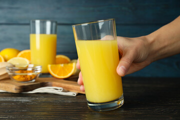 Glasses with juice, hand and ingredients on kitchen board on wooden background, close up
