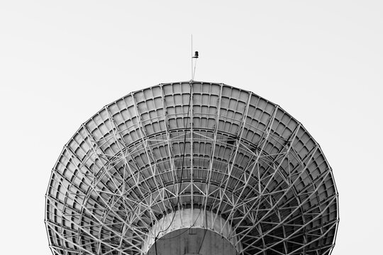 Black and white picture of a radio telescope giant paraboloid surface in morning sunlight under sky