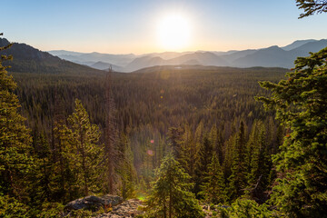 Sunrise over a vast forested valley in the mountains during early morning hours with distant peaks
