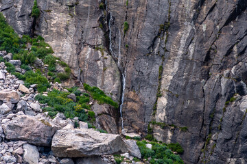 A small waterfall cascades down rocky cliffs surrounded by lush greenery in a remote mountainous area during daylight