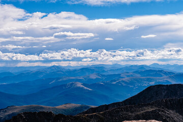 Expansive mountain view during midday with blue skies and layered peaks under a dramatic cloudscape...