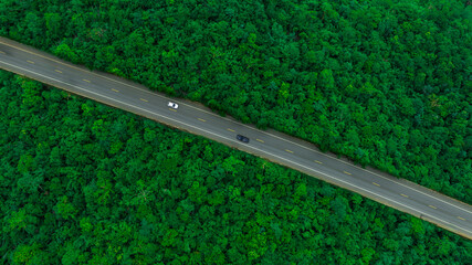Aerial view of dark green forest road and white electric car Natural landscape and elevated roads...