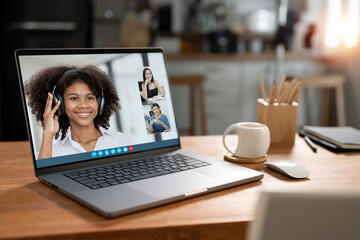 Laptop computer with people meeting online video conference screen display on wooden table in home office.