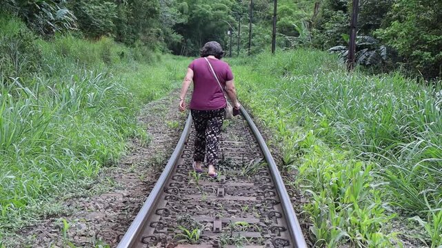 Uma mulher idosa caminhando na linha do trem em &aacute;rea rural