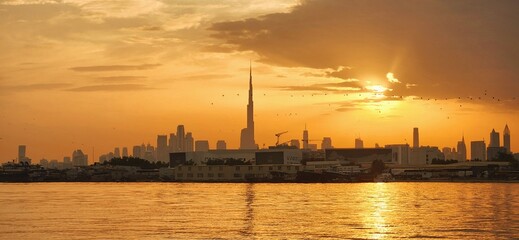 Naklejka premium Orange sunset in Dubai. View the city center, Burj Khalifa, and the river. Cloudy sky.