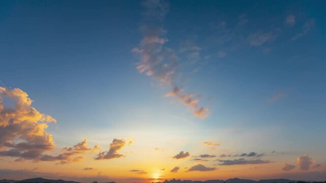 A time lapse of sunset with sun rays piercing through scattered clouds against a clear blue sky