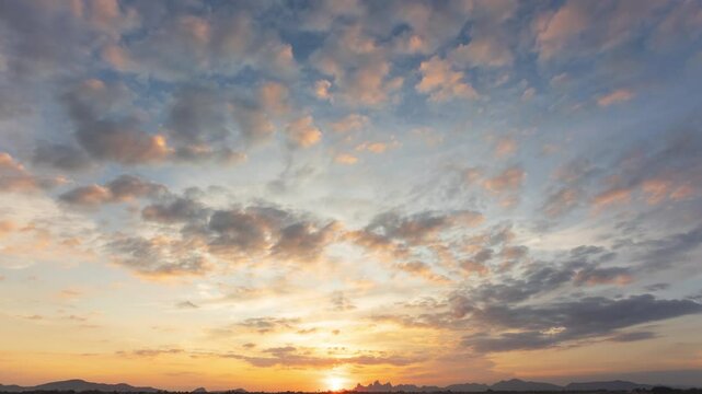 A time apse of sunset with sun rays piercing through scattered clouds against a clear blue sky