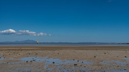 The low tide in the ocean. Puddles of water on the exposed sandy seabed. A sailing boat in the distance. Mountains on the horizon against the blue sky and clouds. Copy space. Madagascar. Nosy Be 