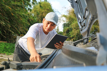 A young mechanic opens the hood of a car to check for engine damage and perform professional maintenance. He wears a grey uniform and inspects and repairs his car in the maintenance center.