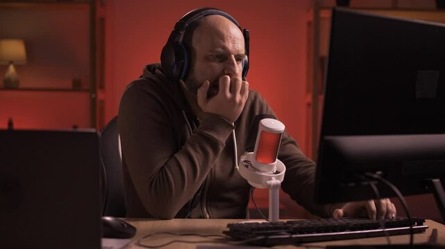 Nervous streamer man playing online competition at professional microphone in gaming room. Millennial gamer bite nails playing online video games and streaming during tournament