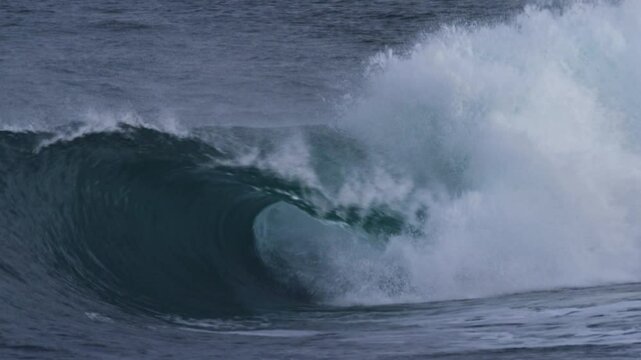 Atlantic wave barrels smoothly, rolling forward in slow motion under stormy skies