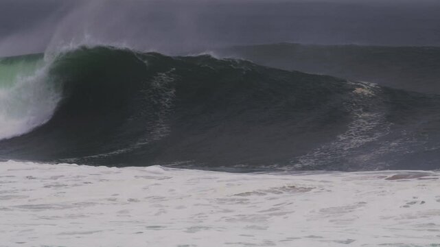 Huge wave crashes, mist streaming off as it barrels during a stormy, blue-lit sunset
