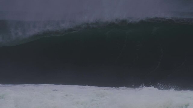 Huge wave forms a dramatic barrel, mist trailing off the peak under stormy blue skies