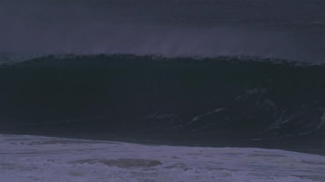Large wave curls into a deep barrel, mist trailing off the top in dark blue hour hues