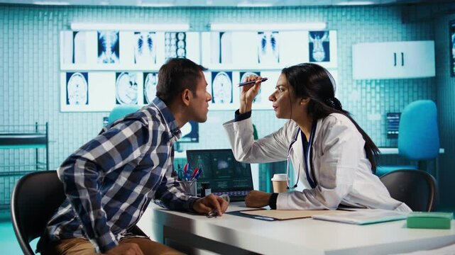 Ophthalmologist conducts eye exam for indian patient in cabinet. Healthcare provider using modern optical equipment for vision correction, eyesight diagnostics in a medical office. Camera B.