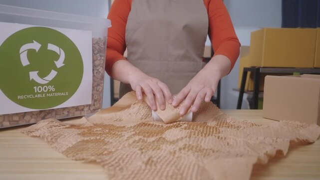 A woman wraps a product with eco-friendly honeycomb paper with label stating "100% Recyclable Materials" highlighting the sustainable practices of a small business. Slow Motion