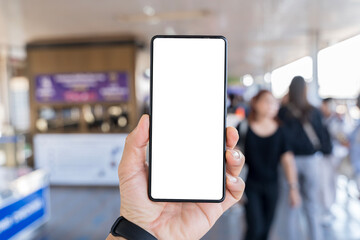 Man's hand holding mobile phone with white empty screen in front of blurry subway