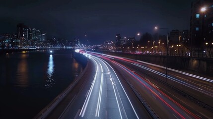 Obraz premium A sense of anticipation as car light trails mark the path along the riverside road leading to the brightly lit city ahead.