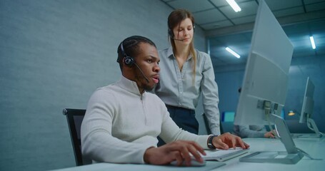 Modern call center office: Two multiethnic technical support specialists wearing headsets talk, discuss work monitoring data on computer. Team of hotline operators working in online customer support. - Powered by Adobe