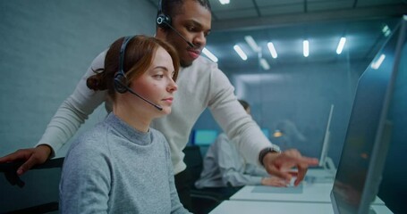 Modern call center office: Two diverse technical support specialists wearing headsets talk, discuss work monitoring data on computer. Team of hotline operators working in online customer support. - Powered by Adobe