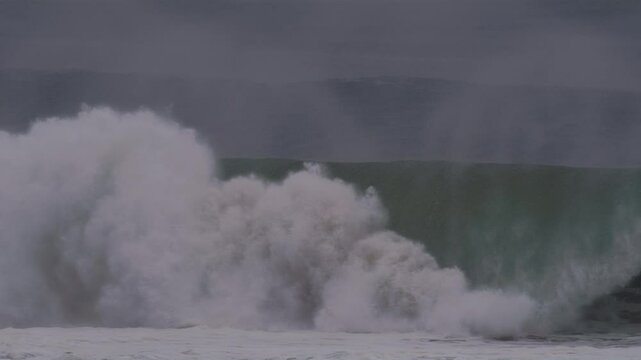 Slow motion wave curls into a barrel, with mist streaming off during stormy blue sunset