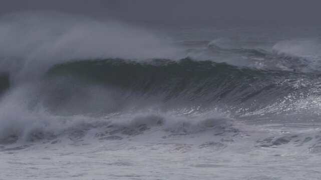 Giant wave forms a hollow barrel, with mist trailing off the top at blue hour