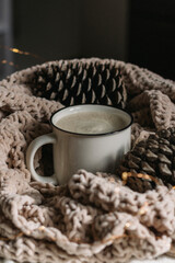 New Year, Christmas card. Coffee with milk in a white mug among the cones wrapped in a warm knitted blanket. Cozy still life