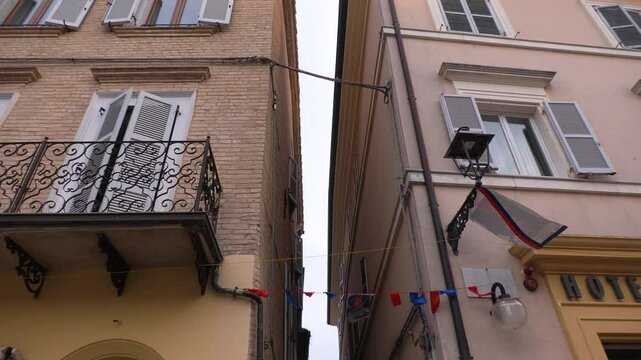 Narrow street with balconies near Loretto Sanctuary, Italy, historic Italian architecture view, upward angle as flags wave in wind