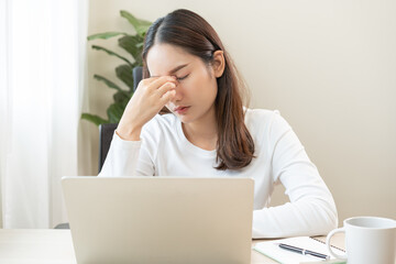 Tired asian young woman burnout, stressed from problem work at desk in office, looking at laptop computer, feeling sick, pain eye strain rubbing dry irritated eyes fatigued working late on deadline.