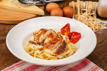 Homemade pasta with grilled chicken.Italian dish Handmade pasta served in a white pasta dish garnished with dried tomatoes.