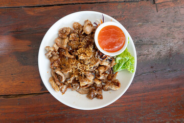 Food of Thailand Fried Pork with Garlic. Served with a slightly spicy dipping sauce. Place on a white plate and place on a wooden surface.